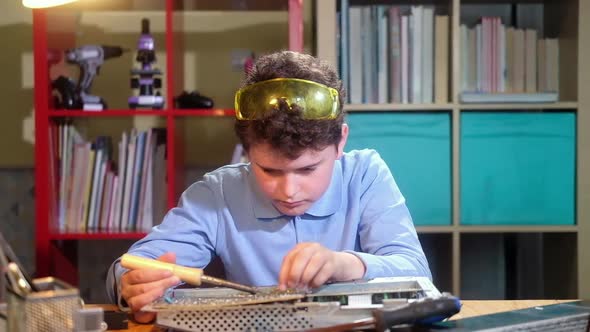 Schoolboy boy solders chip and watches video with instructions in laptop