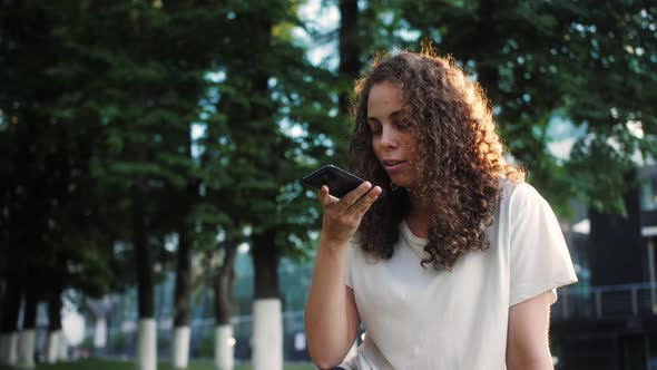 Young Mixed Race Young Woman Holding a Mobile Phone and Recording a Voice Message alt