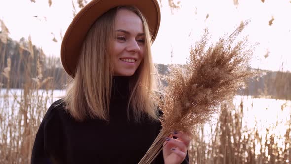 European Blonde Woman Blowing on Pampas Grass with Beige Hat in Black Sweater in the Countryside alt