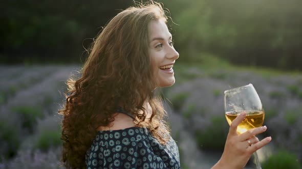 Cheerful Caucasian Woman in Dress Holding Glass of Wine on Field Outdoors Satisfied with Sunny Day