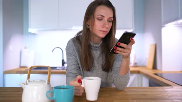 Caucasian Woman Having Breakfast in the Kitchen and Using a Smartphone alt