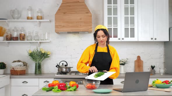 Woman in Kitchen Knives Sliced Cucumber From Cutting Board Into Glass Salad Bowl alt