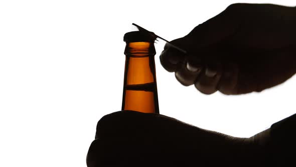 The Silhouette of Male hands opening brown beer bottle with opener