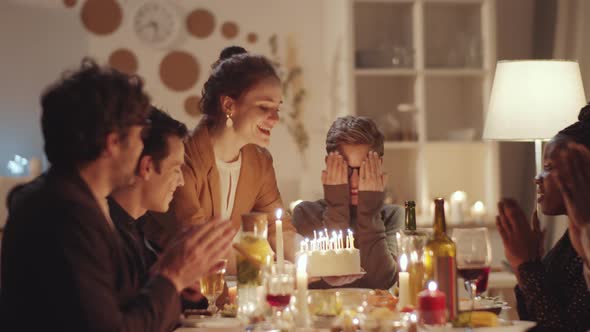 Happy Woman Blowing Candles on Birthday Cake at Dinner Party alt