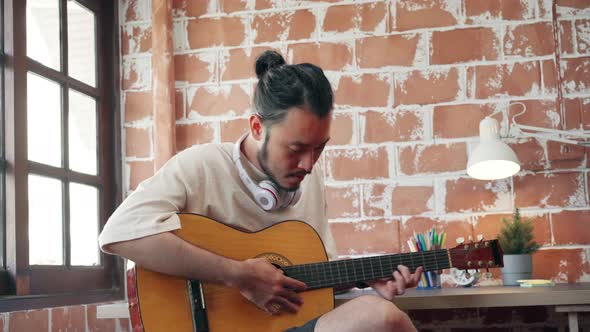 Asian man playing guitar and singing in living room at home. alt