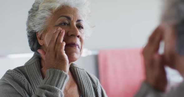 African american senior woman applying face cream while looking in the mirror at home alt