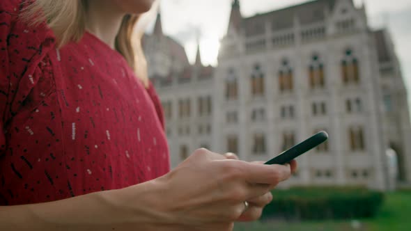 Woman in Red Dress Uses Mobile App on Smartphone By Budapest Parliament Building
