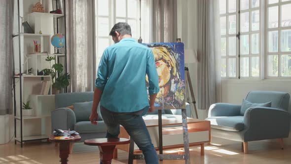 Hind View Of An Asian Artist Man Coming To Sit And Painting A Girl On The Canvas alt