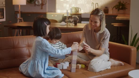 Happy Asian Young Mother and Two Little Children Sitting at Sofa and Playing Together alt