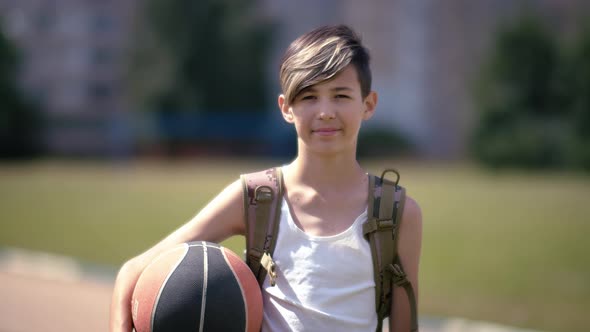 Teen Boy with a Basketball Looking at the Camera and Smiling Summer Sunny Day