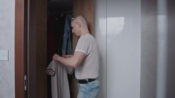 Young Millennial Nonbinary Queer Person in Mesh Tshirt Looking for Clothes in a Closet with Wooden alt