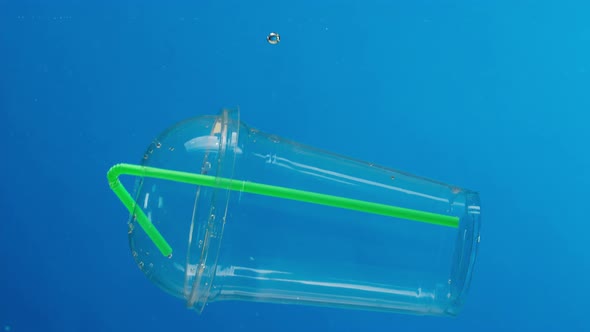 Sinking Plastic Glass with a Cocktail Tube in the Ocean Throwing Garbage Into the River or Lake alt