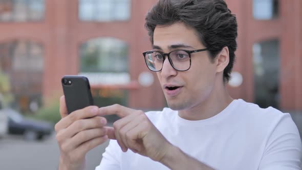 Outdoor Portrait of Young Man Cheering Success on Smartphone alt