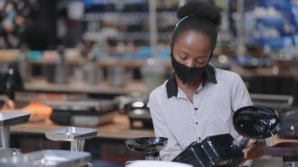 Young Black Woman with Face Mask is Shopping in Hardware Store Choosing Home Appliances Viewing alt