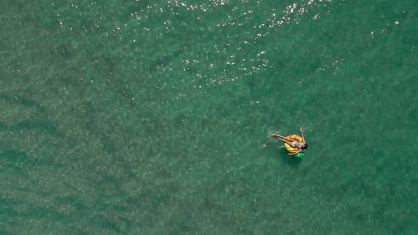 Aerial Top View of Turquoise Sea Water and Woman Swimming on the Yellow Swim Ring alt