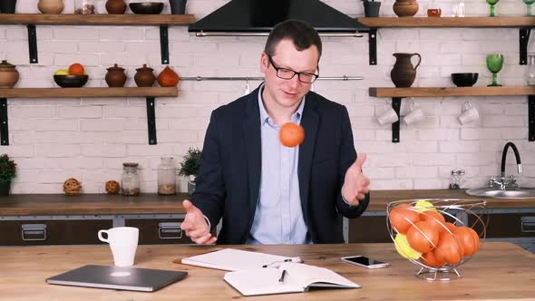 Relaxed Male Entrepreneur in Business Suit and Glasses Throws an Orange From Hand to Hand While