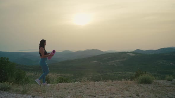 Girl with a Mat Goes to Do Yoga in the Mountains at Sunset alt