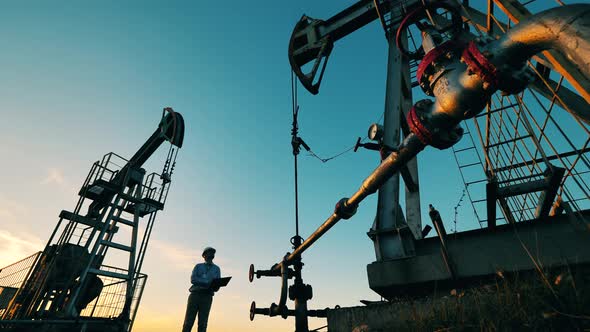 Engineer with Laptop Controls Oil Extraction Between Two Oil Pumpjacks alt