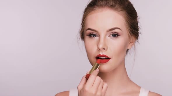 Attractive Woman Applies Red Lipstick and Smiles Isolated on Grey alt