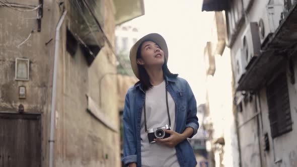 Smiling of female young Asian traveler wearing retro fedora hat walking. alt