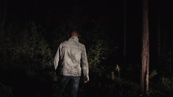 A Man Stands with His Back Turned at Night in the Forest Looking Around alt