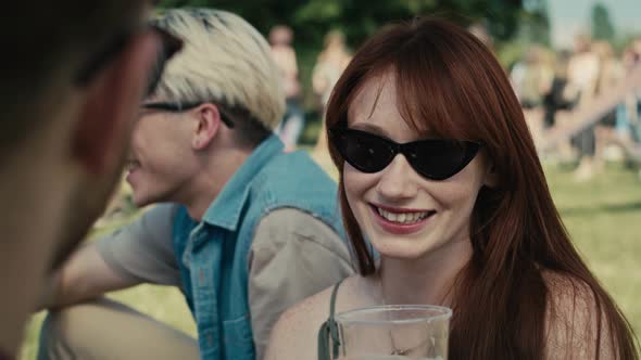 Close up of caucasian ginger hair woman drinking beer from disposable cup at music festival and chat alt