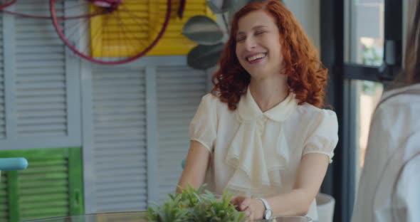 Two young business women colleagues laughing during a coffee break in a colorful boutique cafe. alt