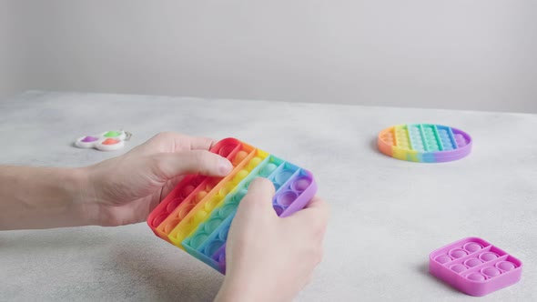 Man Playing Pushing Bubbles on Trendy Rainbow Poppit Fidget Toy with Fingers