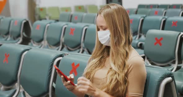 Young Woman in Mask Waiting Flight in Empty Airport Departure Room