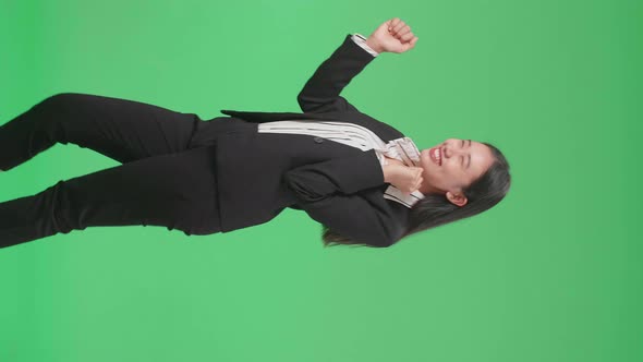 Side View Of A Smiling Asian Business Woman Dancing While Standing On Green Screen Background alt