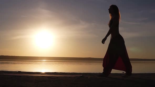 Silhouette of a Fit Woman Near the Water Unfolds the Yoga Mat Preparing Doing Yoga or Pilates alt
