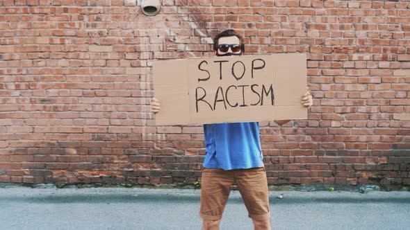 Man in Mask Stands Against Red Wall with Cardboard Poster  STOP RACISM