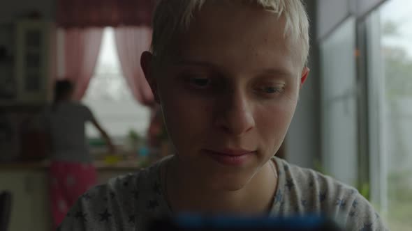 Teenager At Home At Table On Background Of Window Communicates By Video Chat alt
