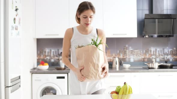 Beautiful Young Caucasian Female Coming to Kitchen with Grocery Shopping Bag and Taking Out alt