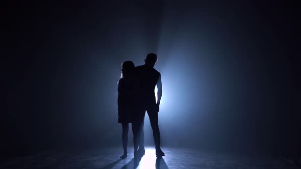 Silhouette of Couple Dancers Against Spotlight with Haze at Dark Studio alt