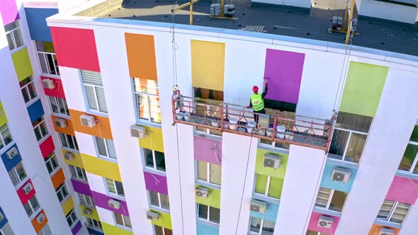 A Worker Paints A Building At A Height.