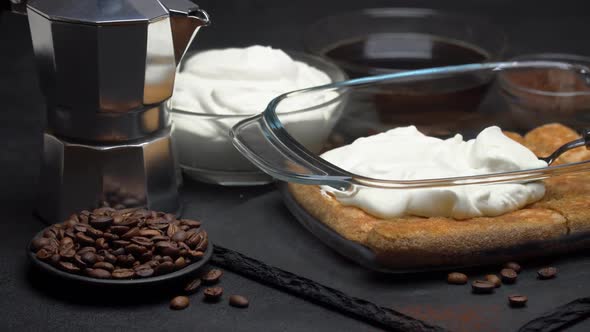 Savoiardi Ladyfingers Biscuits and Cream in Baking Dish, Coffe Maker on Dark Concrete Background alt