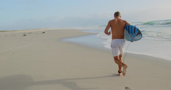 Male surfer running on the beach 