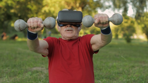 Senior Old Grandfather Man in VR Headset Helmet Making Fitness Exercises with Dumbbells in Park alt