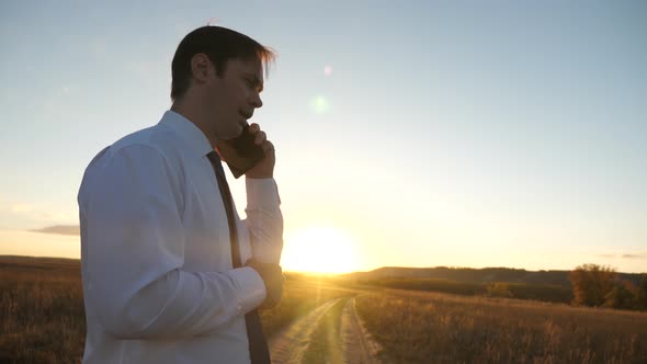 Businessman Talking on a Smartphone Against the Sky. Man in a Tie with a Tablet in the Park alt