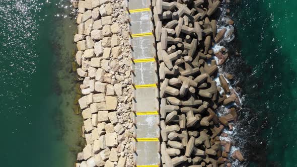 Small blue waves from the clear Mediterranean sea splash on the man-made pier with large unusually s alt