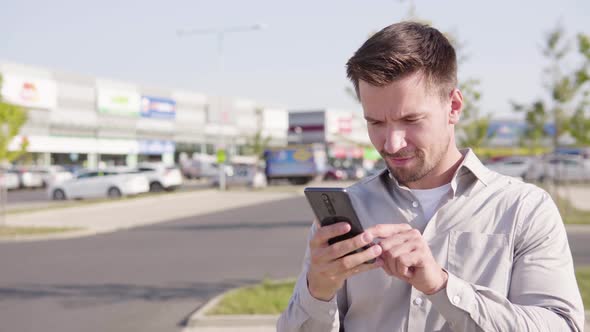A Young Caucasian Man Takes Selfies with a Smartphone in an Urban Area alt
