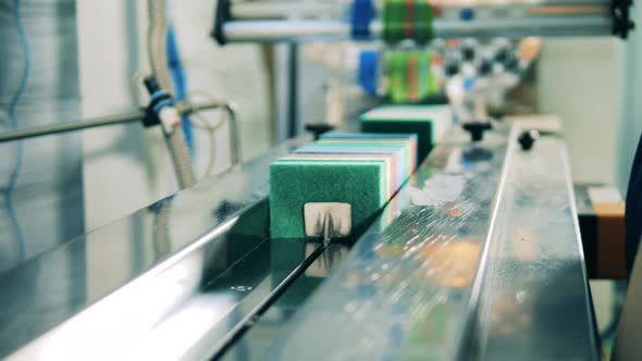 Factory Worker Loading Scrub Sponges Onto a Conveyor Belt at a Factory alt