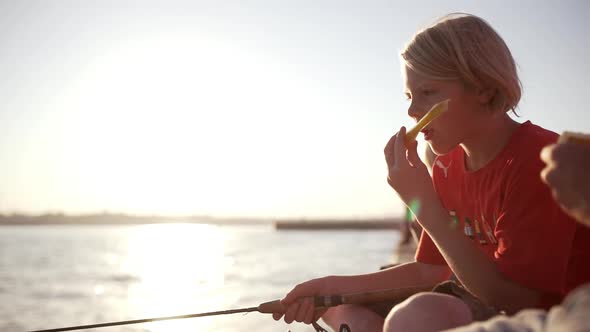 Young Caucasian Kid in Red Tshirt Fishing Sitting on Pier Eating Melon in Slowmotion alt