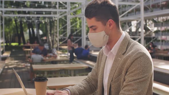  Businessman in Face Mask Working on Laptop in Cafe alt