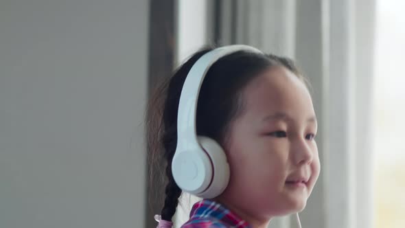 Little Asian Girl in Headphones Dancing with Smartphone at Home