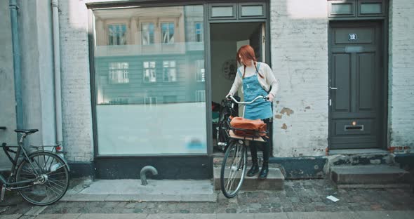 Young redhead woman ready to leave the house with a bike alt