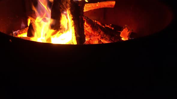 Campfire flames burn firewood bright orange during night at outdoor campsite. alt