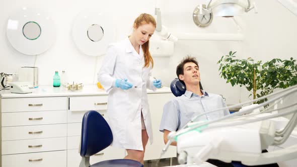 Female Dentist Examining Teeth of Young Man with Mirror During Dental Checkup in Medical Clinic alt