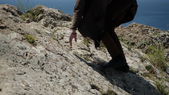 a Young Man with Long Hair Climbs Up the Cliff Up To the Top of the Mountain alt